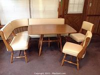 Full view of vintage mid century dining set with corner bench and two chairs around rectangular wooden table with cream upholstered seats.