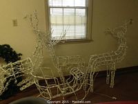 Photo of two large white lighted wireframe reindeer decorations near a window indoors.