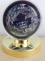 Front and side view of signed Toronto Maple Leafs hockey puck inside clear plastic case and gold-colored stand.