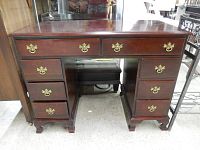 Photo of the front view of the cherry wood desk showing all eight drawers and brass handles.