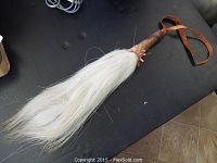 Full length view of African whisk with white hair and leather handle on black background.