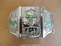 Front view of silver-tone metal skull belt buckle with green enamel eyes and built-in lighter.