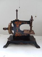 Front angle view of small vintage child's toy sewing machine with painted floral stencil decorations and wooden handle hand-crank wheel