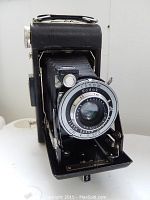 Full front view of the folding camera showing lens, shutter, and bellows