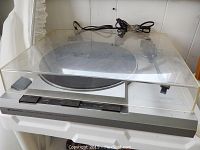Front angled view of Kenwood KD-1600 turntable with clear dust cover, showing tonearm, speed controls, and power cord.