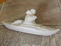 Front-side view of Inuit carving showing the hunter paddling in a kayak with a seal on the back.