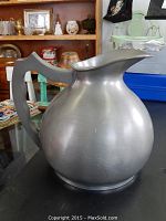 Front and side view of the English pewter water jug on a dark surface with miscellaneous background items.