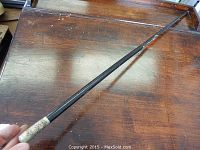 Full length view of the black wooden swagger stick showing some finish loss and a silver engraved cap on the handle.