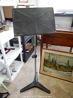 Black metal music stand shown fully upright with adjustable height knob and tripod base visible.
