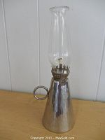 Front view of the hand hammered finger oil lamp showing the hammered metal texture, round finger handle, and clear glass chimney with wick.