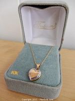 Heart-shaped 10k gold pendant locket and chain displayed in Tradition brand grey velvet jewelry box. The chain is laid out neatly with the pendant centered on the cushion.