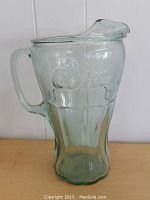 Front view of large clear glass pitcher embossed with Coke logo, showing handle and spout
