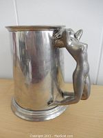 Side view showing tankard body and detailed figural nude female handle in kneeling pose