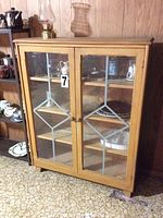 Front view of the solid wood display case with glass doors and metal decorative framing showing overall structure and contents inside.