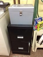 Metal 2-drawer black file cabinet with keys and a gray portable file box on top, showing overall condition and size.