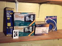Three boxed faucet sets: two large Danze two-handled lavatory faucet sets and one smaller Danze faucet set, plus a BrassCraft toilet tank fill valve in original packaging and a coiled plumbing hose.