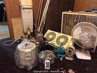 Photo showing variety of fans, deep fryer, steam cleaner, and large brown rolled carpet