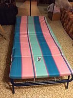 Folded out single fold away bed with striped foam pad in blue, pink, and green stripes on a linoleum floor pattern.
