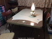 Full view of vintage kitchen table with leaf inserted and a lit electric lamp positioned centrally on top; table top has brown and white starburst design with chrome edged metal legs visible.