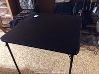 Black folding card table set up, showing top surface and legs