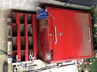 Closed view of large red metal tool box with side compartment organizer and mounted vice. Keys visible on vice handle.