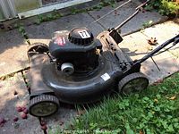 Side angle photo of the gas lawn mower showing the Briggs & Stratton engine, wheels, metal deck, and handle assembly.