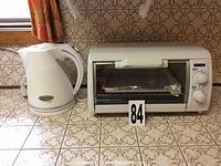 Photo of white Black & Decker toaster oven and white Betty Crocker electric kettle on tiled countertop, showing their condition and design.