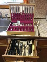 Open case showing eight-piece Oneida silver plated flatware set arranged on red velvet lining. Multiple types of utensils visible including knives, forks, and spoons.