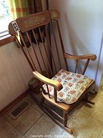 Full view of the solid wood rocking chair with floral motif on backrest and cushioned padded seat.