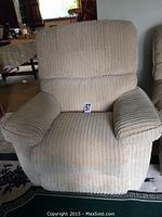 Front view of beige corduroy Lazy Boy rocker recliner, showing cushioned seat, armrests, and backrest with wear signs.