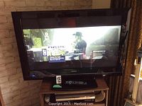 Hitachi 37-inch TV powered on displaying video, remote placed on stand below