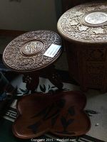 Two round carved wood accent tables side by side showing intricate hand-carved floral and leaf designs on tops and sides.