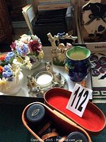 Photo of Scope binoculars in case, bone china flower arrangements, blue ceramic vase, decorative wolf candle, AM/FM radio, and bird field guide on a table.