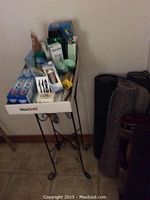 White container holding unopened hygiene products including toothpaste and soap on a wrought iron stand.