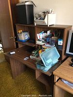 Photo shows a wooden desk and shelving unit loaded with various office supplies, including clear stackable containers, note pads, pens, and more