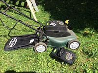 Yardworks cordless lawnmower with grass catcher and spare battery pack on grass