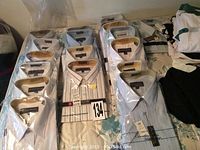 Photo showing multiple men's dress shirts individually wrapped in plastic, mostly in white and light blue colors with collars and some striped designs.