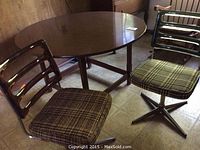 Round wooden kitchen table with veneer surface and two chairs with checkered seats and translucent resin backrests in brown and dark grey.
