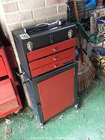 Closed view of black metal toolbox with red drawers and bottom door, showing handle on top and latch locks on lid.