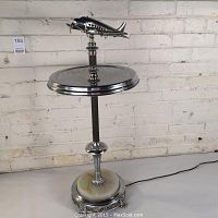 Full view of chrome smoking stand with airplane perched at top over circular tray and slag glass base