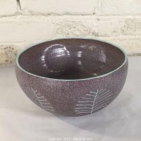 Photo of the bowl showing its rounded shape, purple speckled glaze, white leaf designs, and turquoise rim.