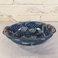 Front view of the oval pottery serving dish showing blue fish motifs and sculpted fish handles with red accents.