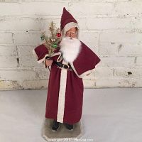Front view of vintage Belsnickle Santa Claus candy container dressed in burgundy felt with fur trim holding decorated feather tree on painted wood base.