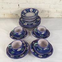 Four cups placed on matching saucers and small plates in front of stacked bowls and plates