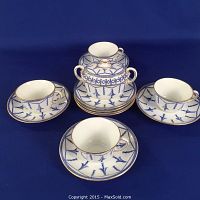 Top view showing four tea cups, eight saucers, and sugar dish with lid, all decorated with blue 'Bells on Chain' pattern and gold trim on white porcelain.