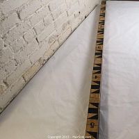 Full length view of the wooden surveyor's stick laid out straight showing hand painted black triangular and number markings on natural wood.