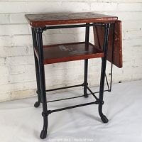 Front angled view of the 1920s stenographer's table showing the wooden top, folding side panel, lower shelf, and black wrought iron frame.