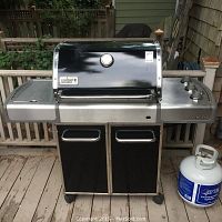 Front view of Weber Genesis grill with enclosed cart and one propane tank at right