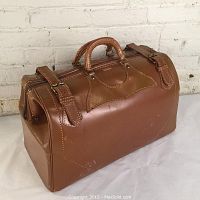 Front view of the vintage brown leather doctor's bag with buckled straps and handles visible.