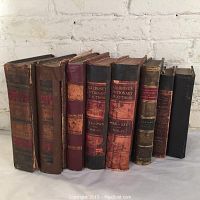 Side view of nine antique books showing various aged leather and cloth bindings